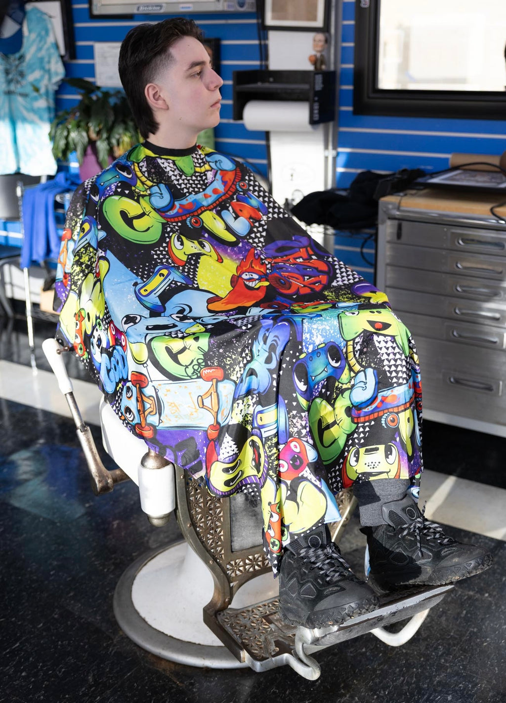 Graffiti Themed waterproof professional barber and salon cape with metal snap closures and unique design including the vibrant colorful style featuring graffiti style gaming controllers skateboards and words play and cool