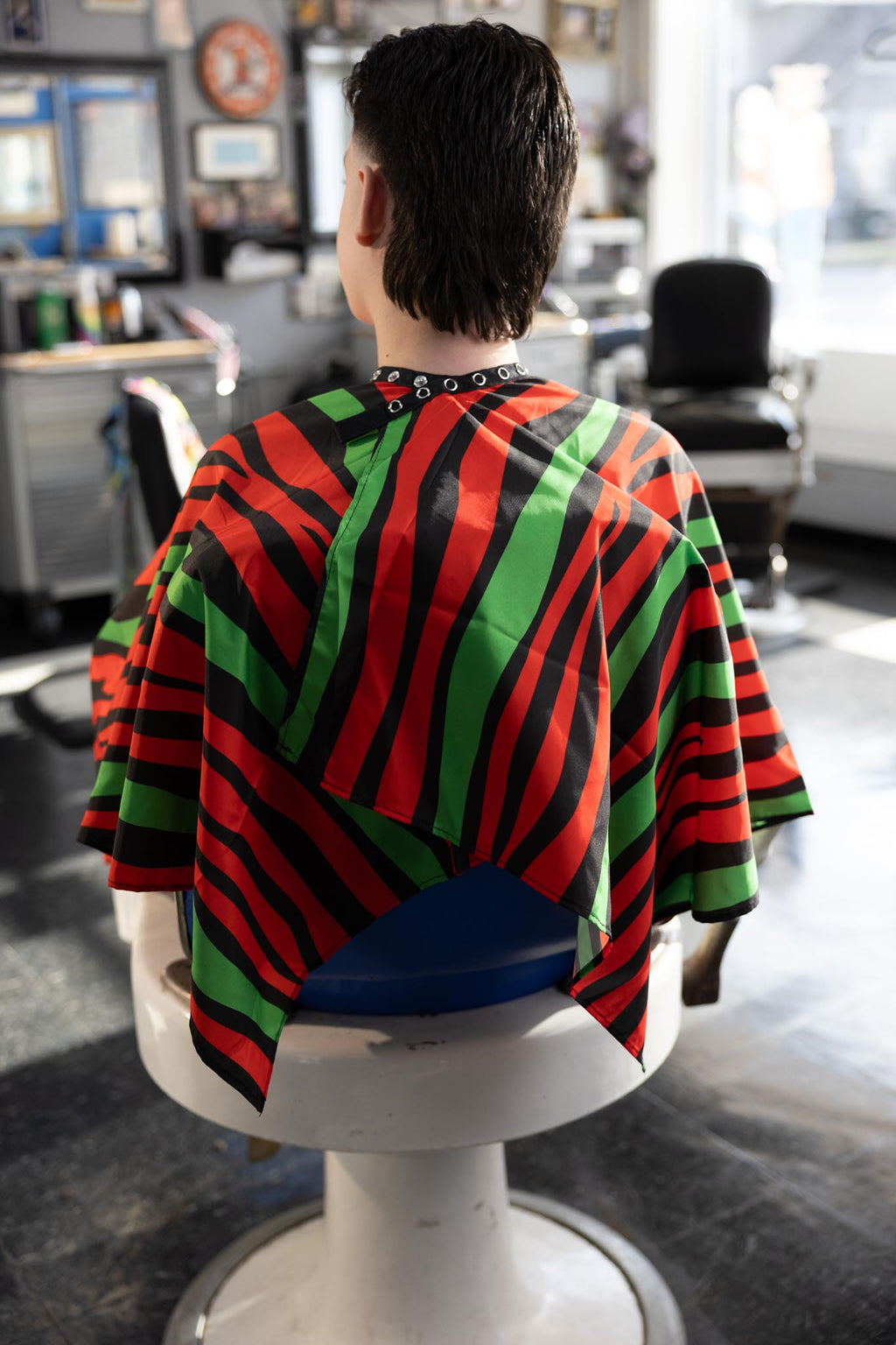 Red Black and Green Striped Themed waterproof professional barber and salon cape with metal snap closures and unique design including the Pan-African style horizontal stripes RBG
